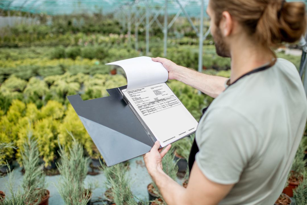 Gardener looking on the folder with plant calendar working in the greenhouse of the plant shop